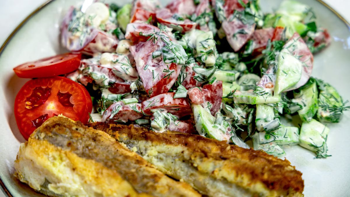 Delicious fresh salad with tomatoes and cucumbers served with a crispy fried fish fillet on a plate.